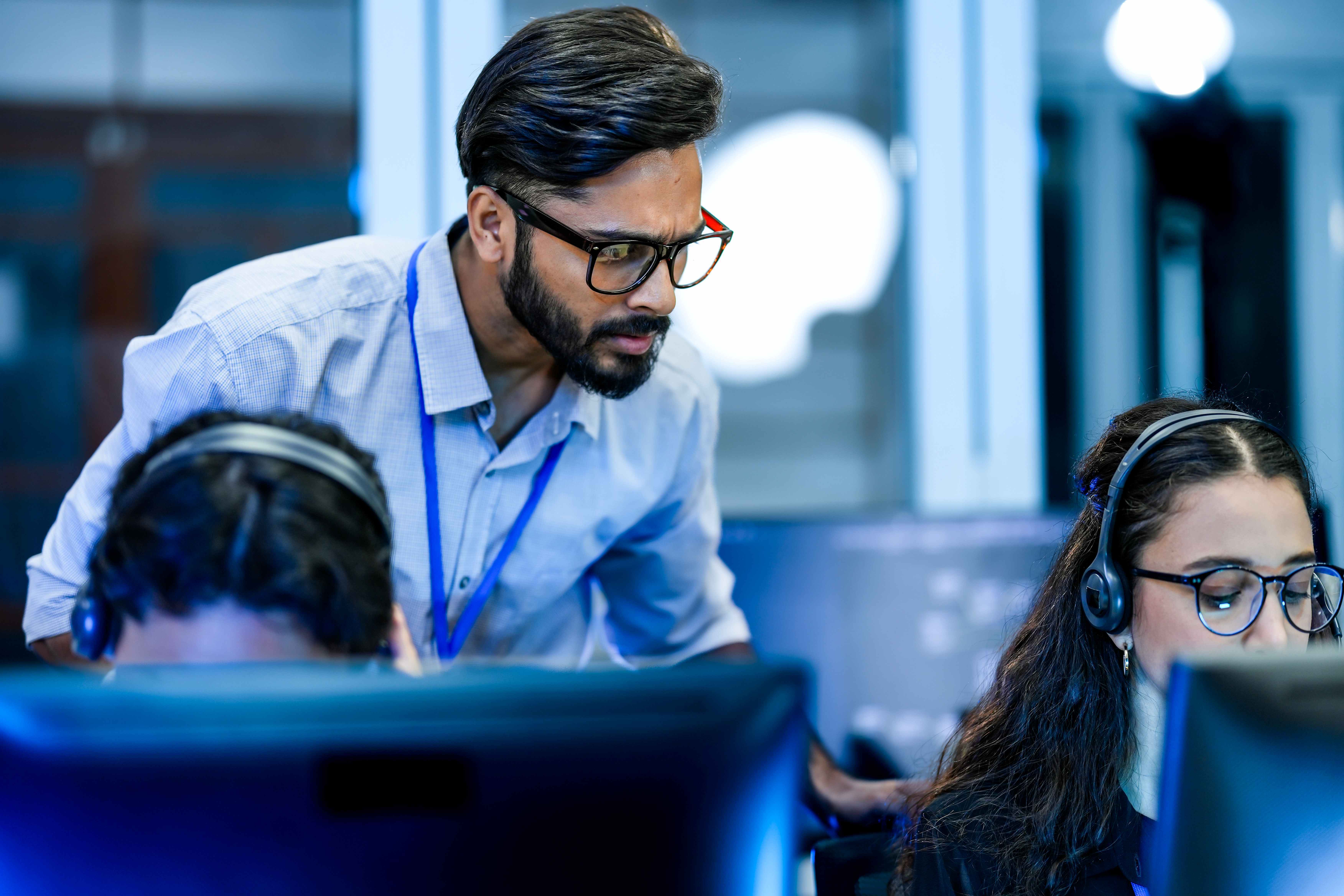 IT helpdesk specialist resolving technical software issues via voip headset. Senior supervisor mentoring support agent on crm interface.