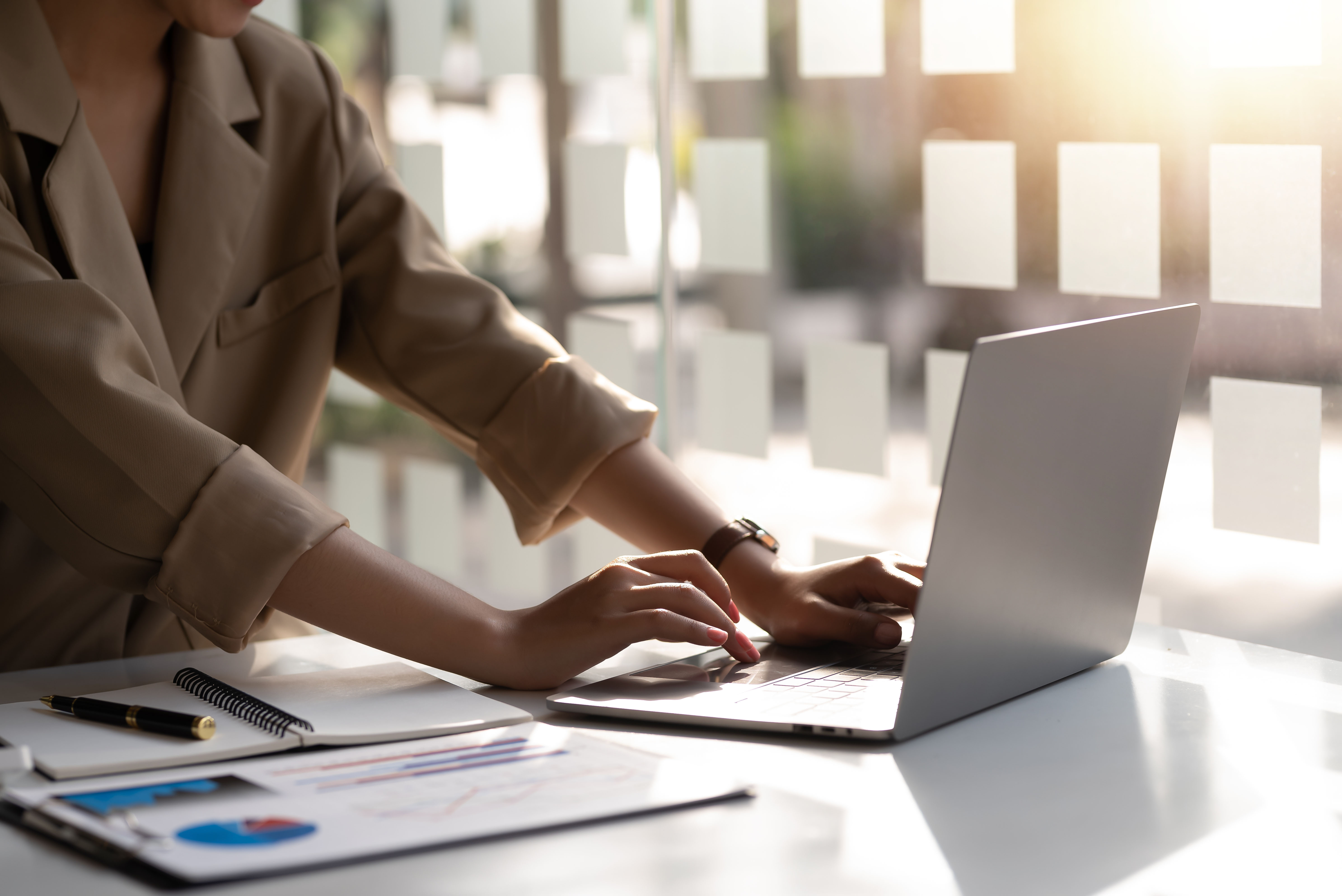 Businesswoman sitting on a laptop computer with documents on the desk in the office.